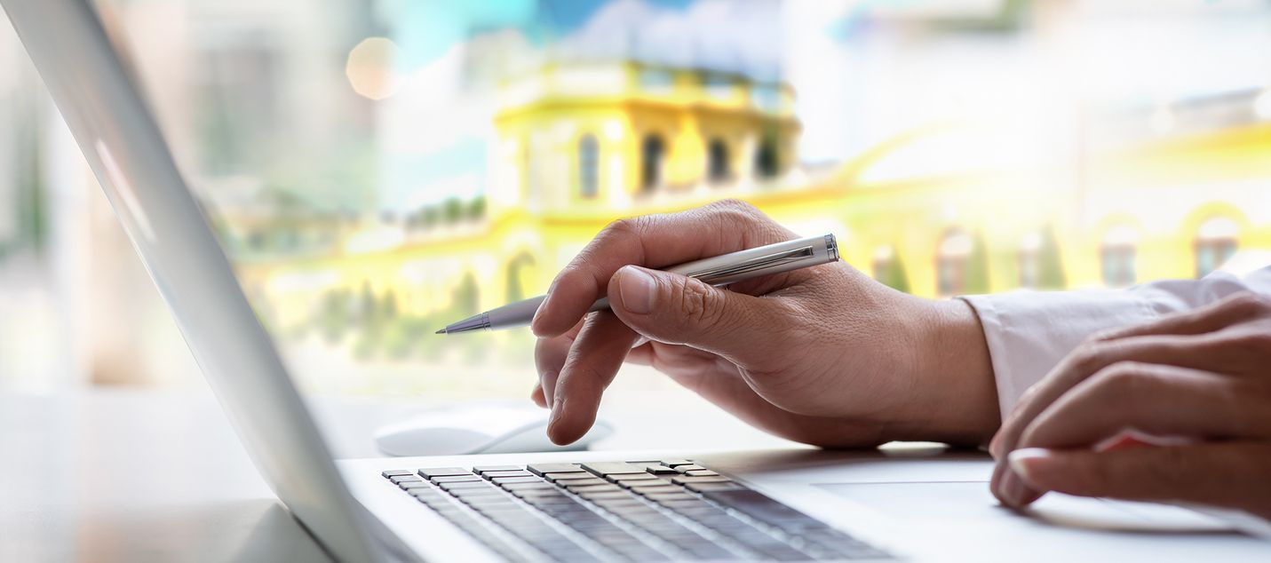 Eine Person nutzt einen Laptop und tippt darauf im Hintergrund ist eine Orangerie im Park Karlsaue in Kassel zusehen